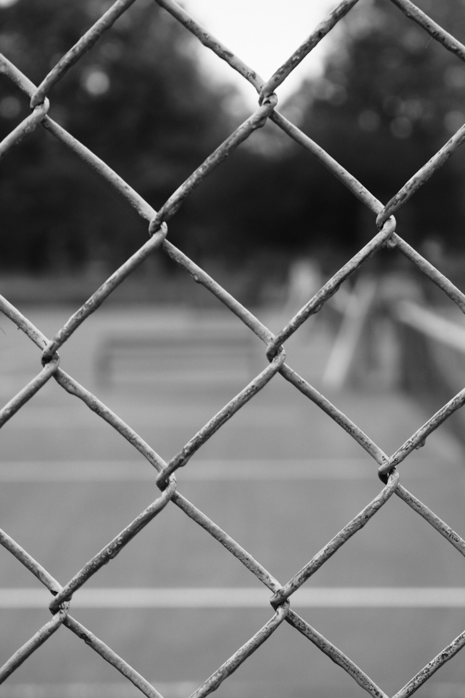 a black and white photo of a tennis court through a chain link fence